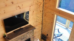 Ein gemütliches Blockhaus-Interieur mit Kamin aus Stein, einem großen Flachbildfernseher, einer dunklen Couch und einem Holzesstisch.