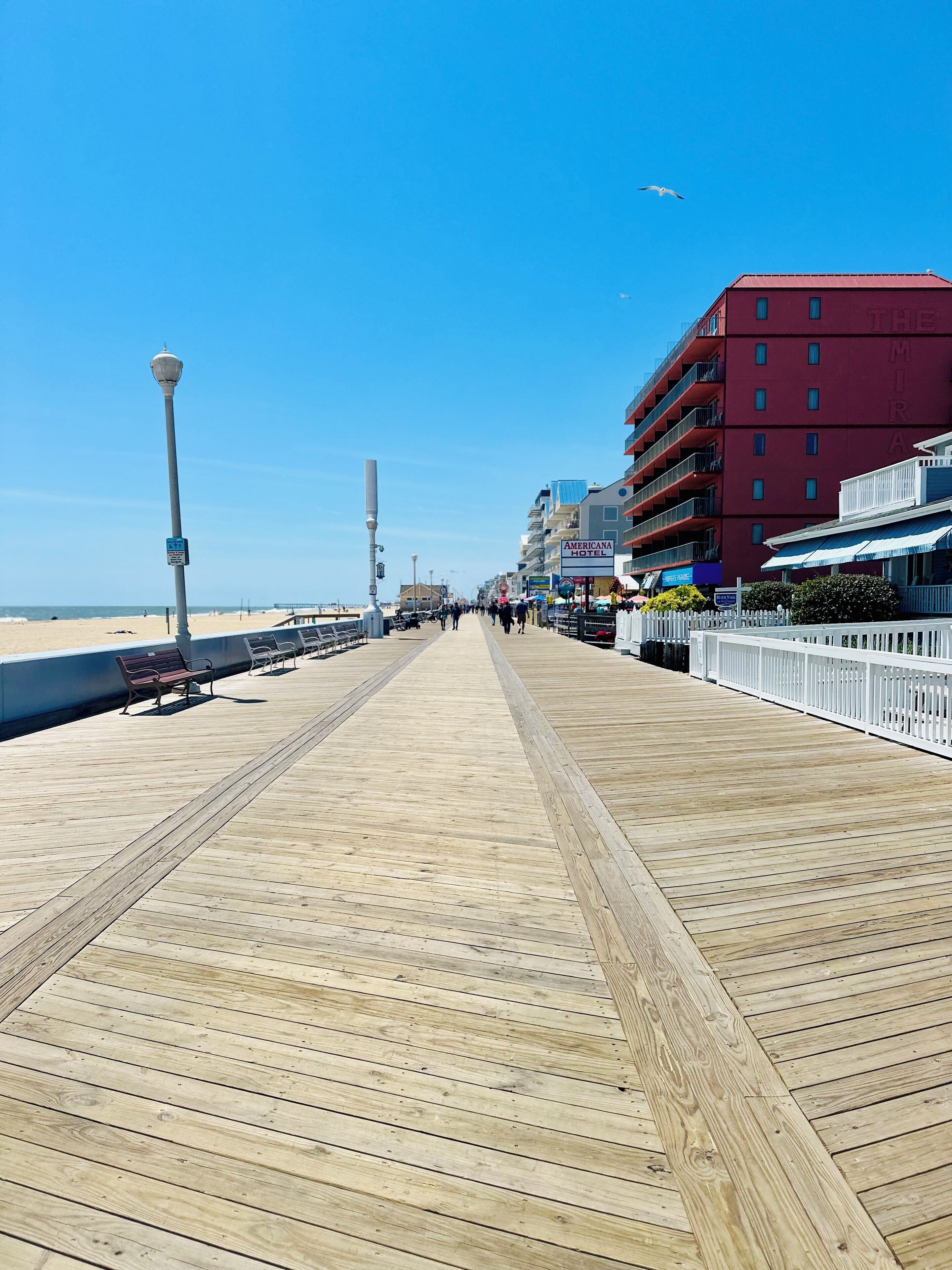 Une promenade en bois avec des bancs, un lampadaire et un bâtiment portant l’inscription « AMERICAN HOTEL », doté de balcons.