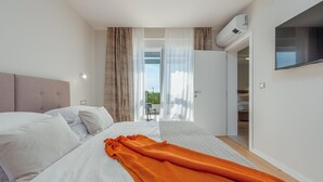 A modern hotel room with a large bed, a TV mounted on the wall, and a balcony with a view. - Beach front home in Sukosan (Sukosan)