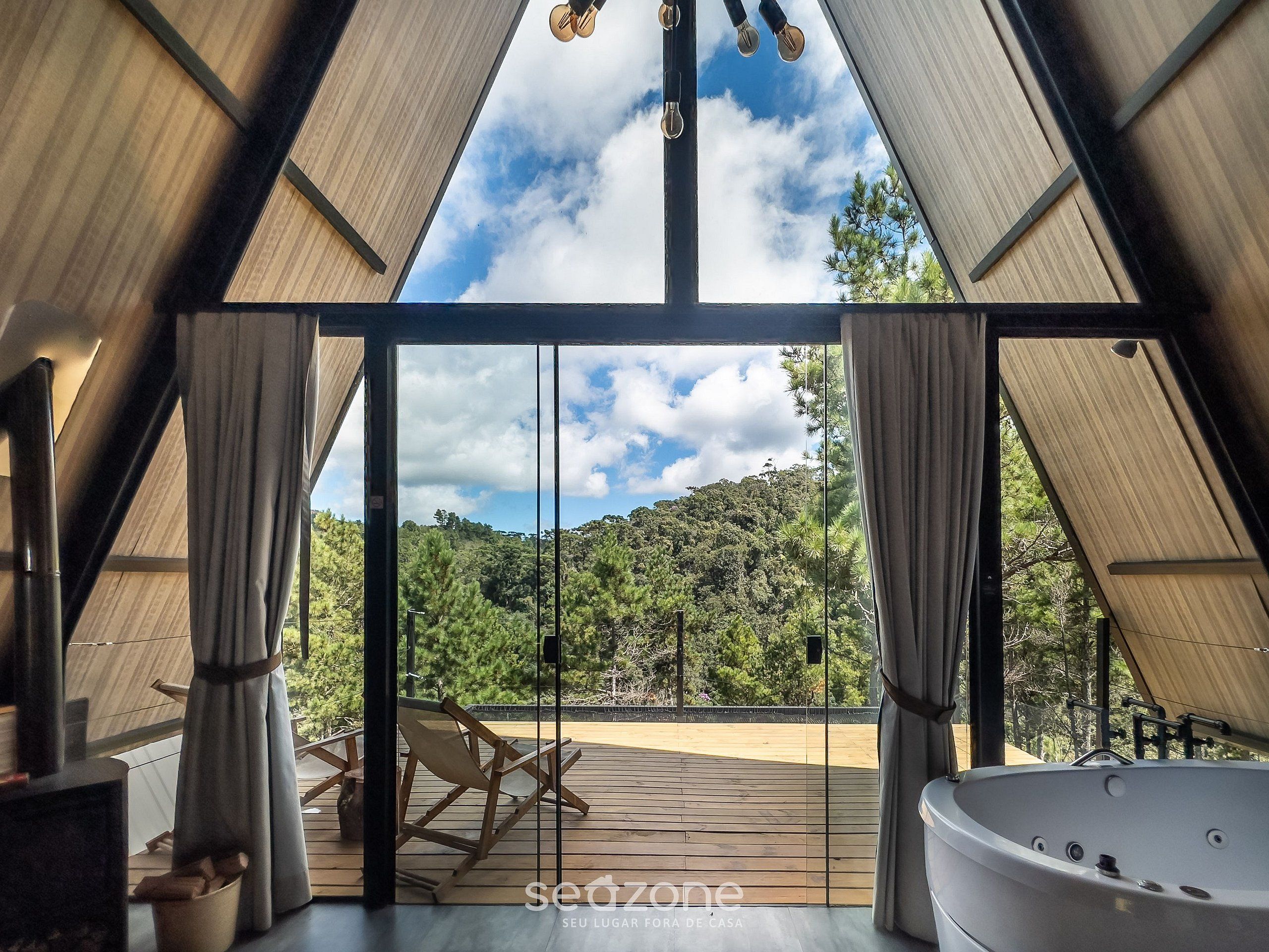 Een modern interieur met een grote glazen deur die uitkomt op een terras, een bubbelbad en uitzicht op een beboste heuvel.