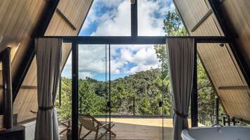 A modern interior with a large glass door leading to a deck, a hot tub, and a view of a forested hillside.
