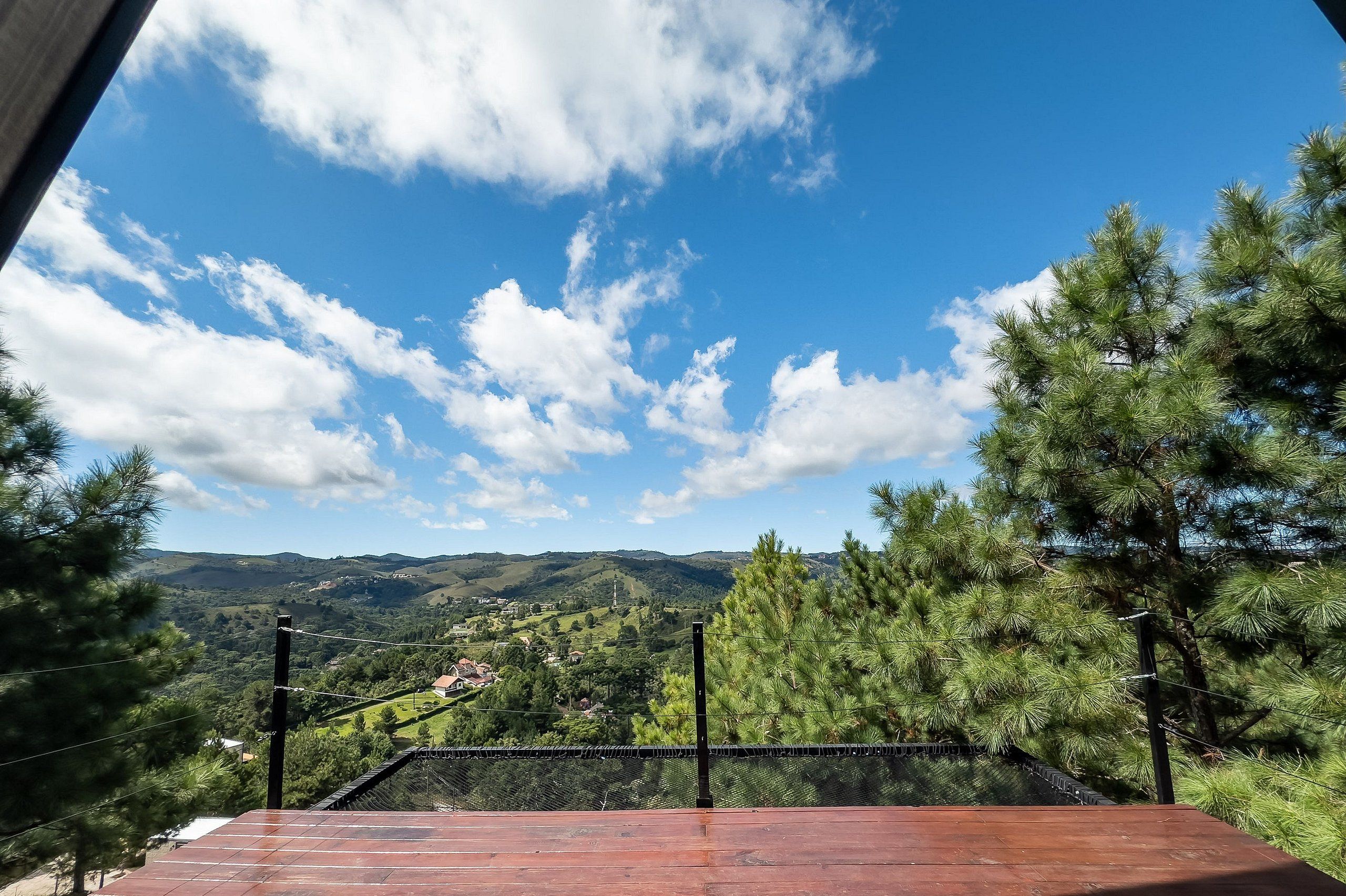 A wooden deck with a view of a hilly landscape, a fence, and a clear blue sky with clouds.