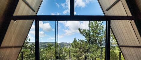A modern interior with a large glass window offering a view of a wooden deck and surrounding greenery.