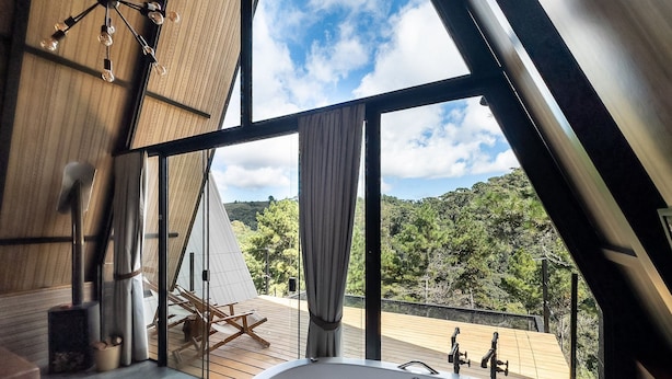 A modern interior with a large skylight, wooden deck, and a view of a forested landscape. - Chales Naturale - Campos do Jordão - CNA (Campos do Jordão)