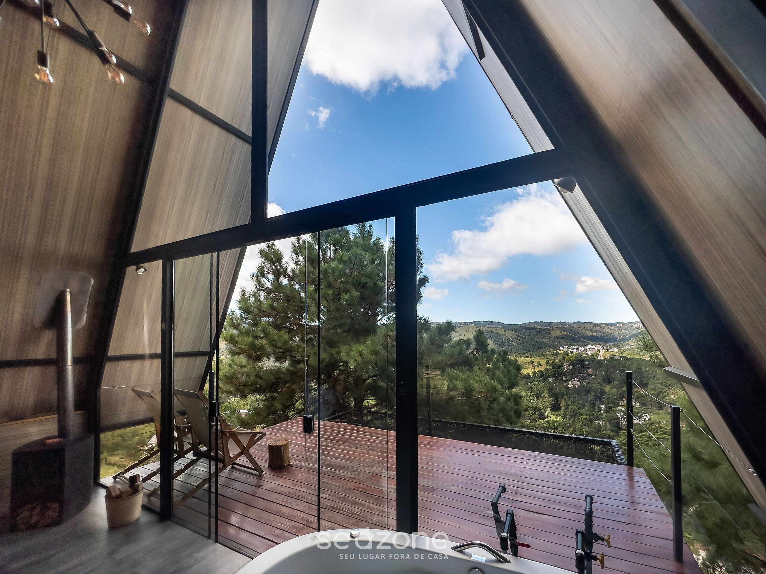 A modern interior with large windows, a wooden deck, and a view of a mountainous landscape.