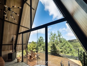 Un interior moderno con un ventanal grande, terraza de madera y vistas a árboles.