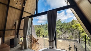 A modern interior with a large window, a wooden ceiling, and a view of the outdoors. - Chales Naturale - Campos do Jordão - CNA (Campos do Jordão)