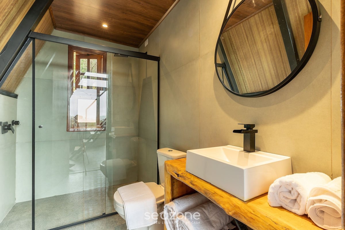 A modern bathroom with a glass shower enclosure, a wooden vanity with a sink, and a round mirror.