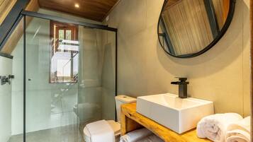 A modern bathroom with a glass shower enclosure, a wooden vanity with a sink, and a round mirror.