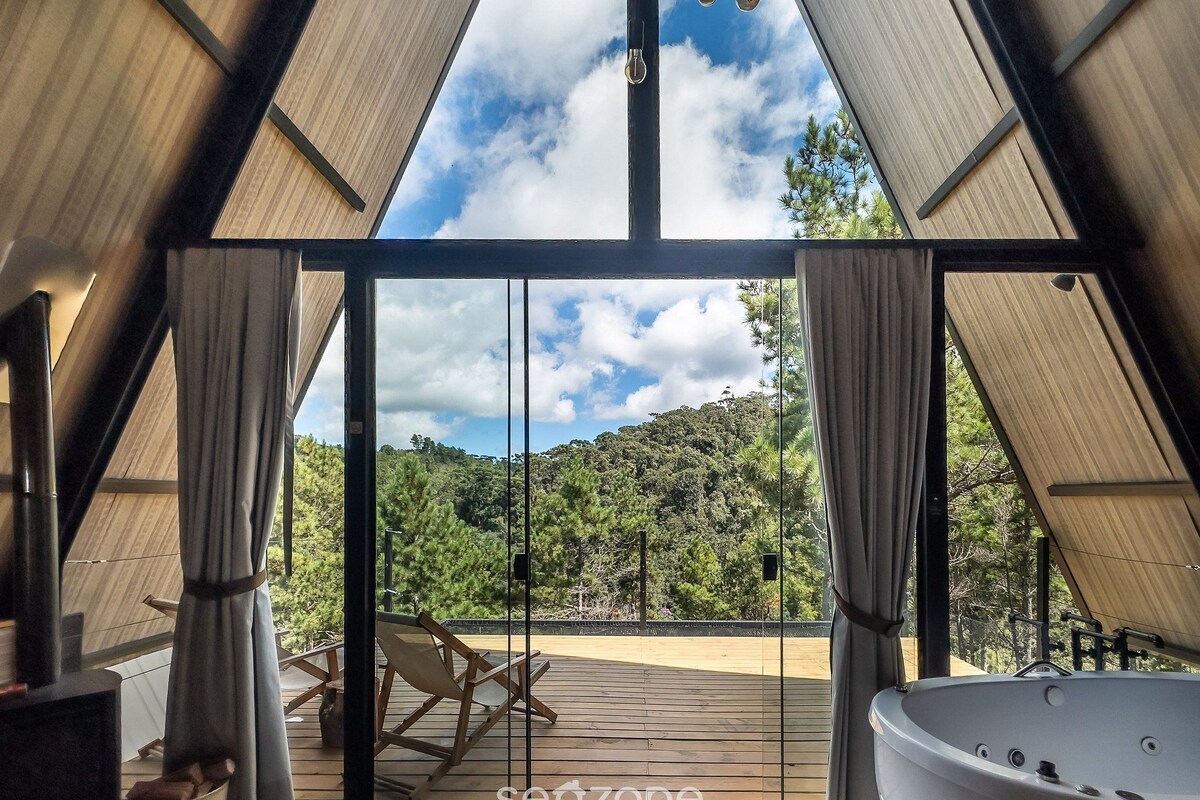 Ein modernes Interieur mit einer großen Glasdoor, die auf eine Terrasse führt, einem Whirlpool und Blick auf einen bewaldeten Hang.