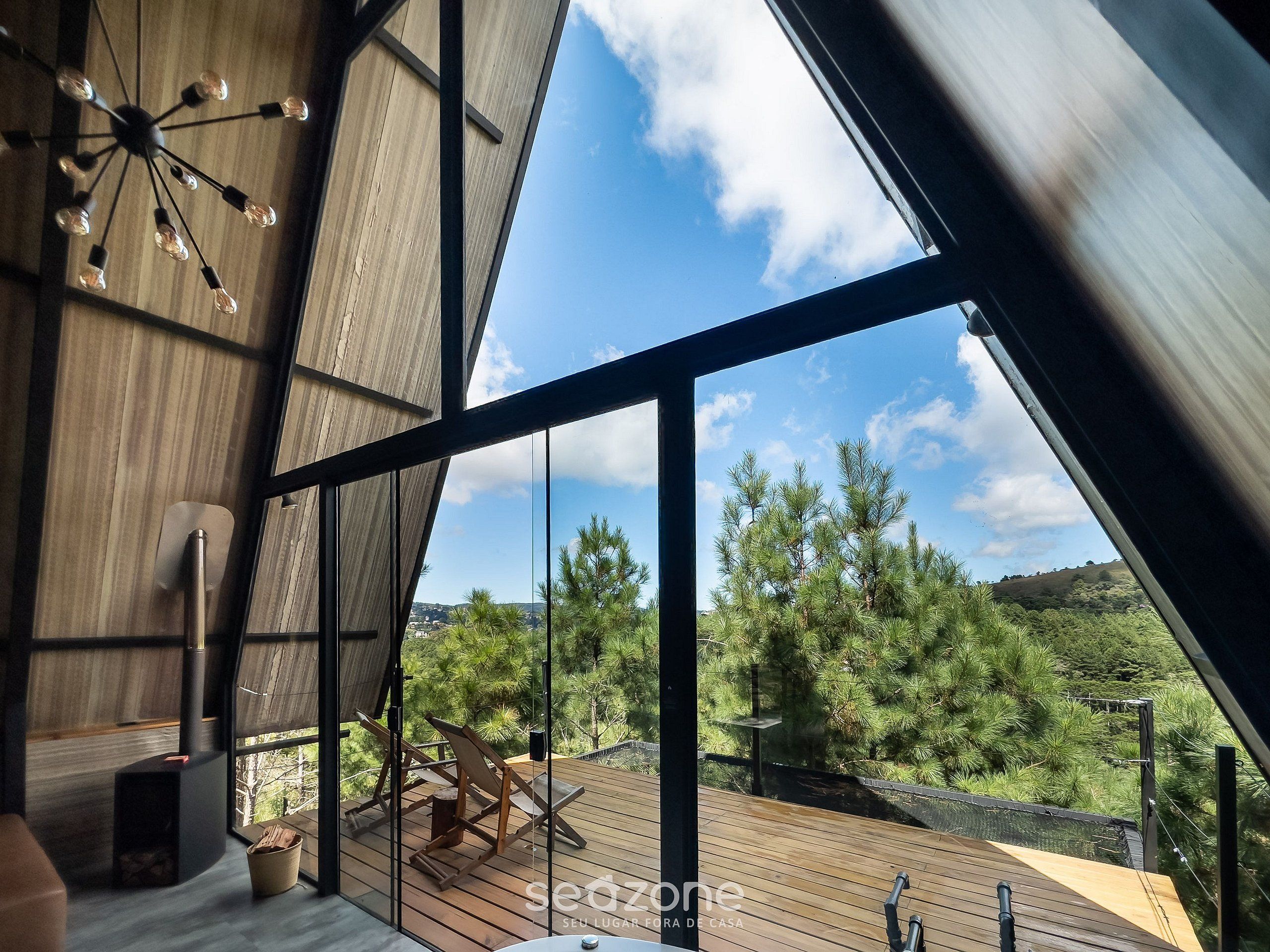A modern interior with a large window, a wooden ceiling, and a view of a deck with outdoor furniture.