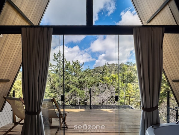 Una habitación con terraza de madera, cortinas y vistas a árboles y al cielo.