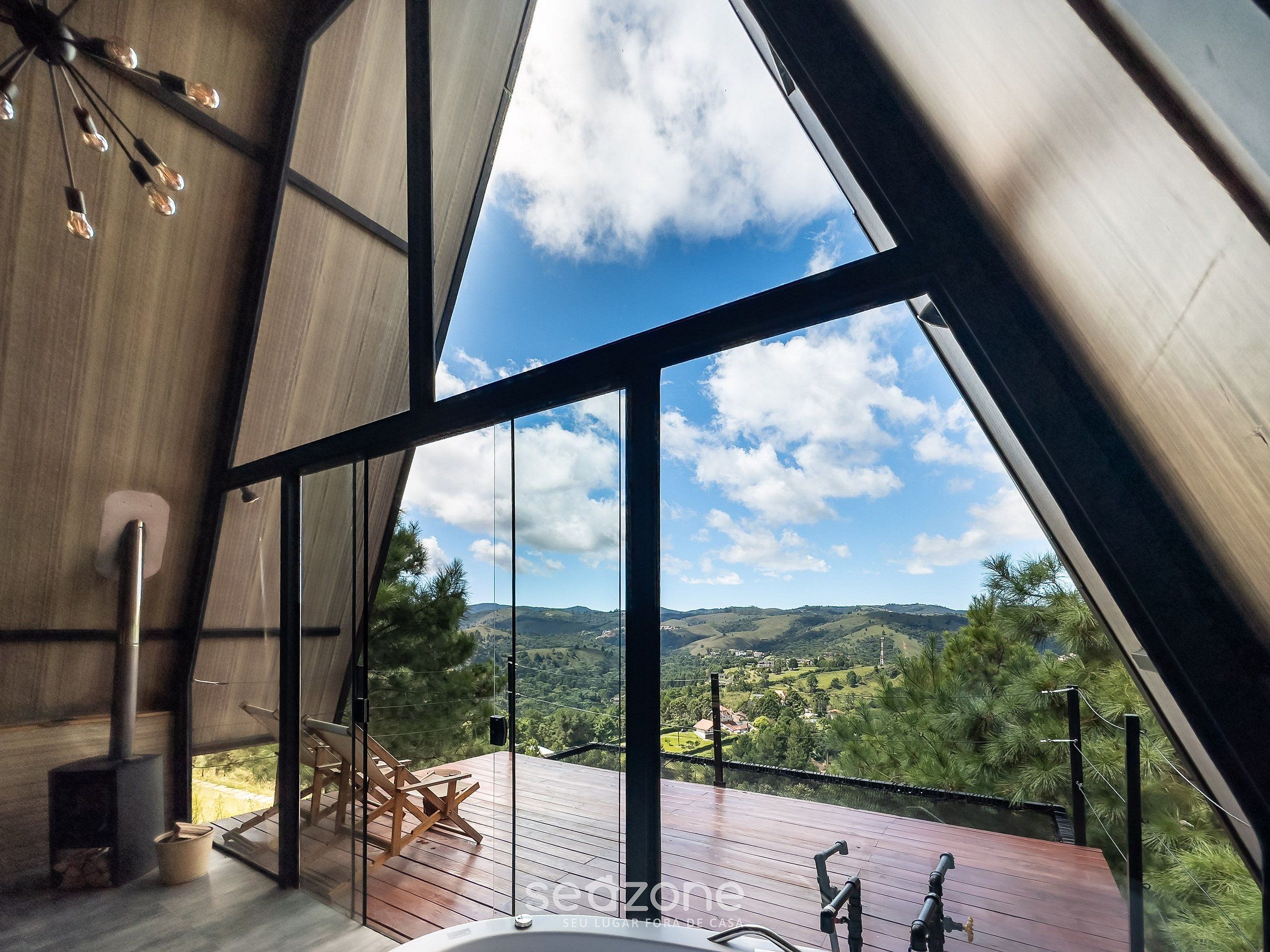 A modern interior with a large window, a wooden deck, and a view of a green landscape.