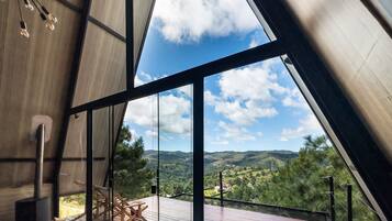 A modern interior with a large window, a wooden deck, and a view of a green landscape.