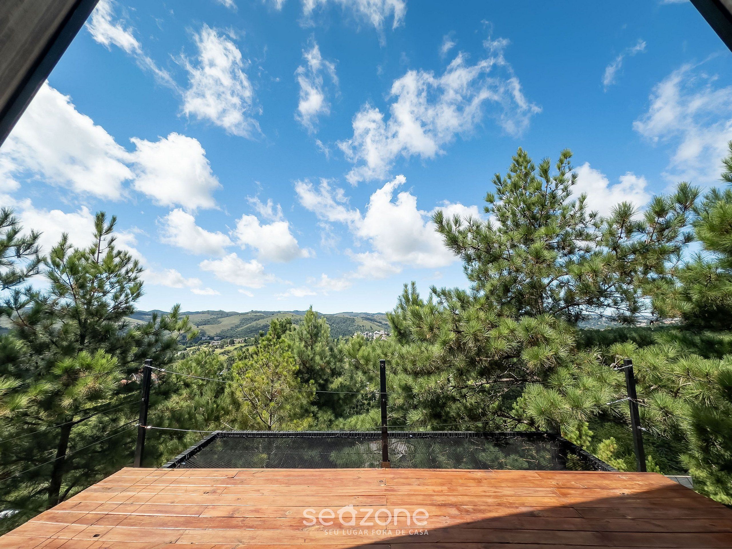 A wooden deck with a view of pine trees and distant hills.