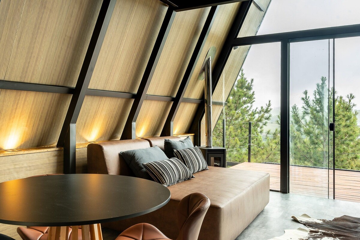 A modern interior with a sofa, a round table, and a view of trees through large windows.