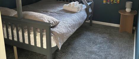 Een slaapkamer met een stapelbed, raam, gordijnen en een klein houten nachtkastje.