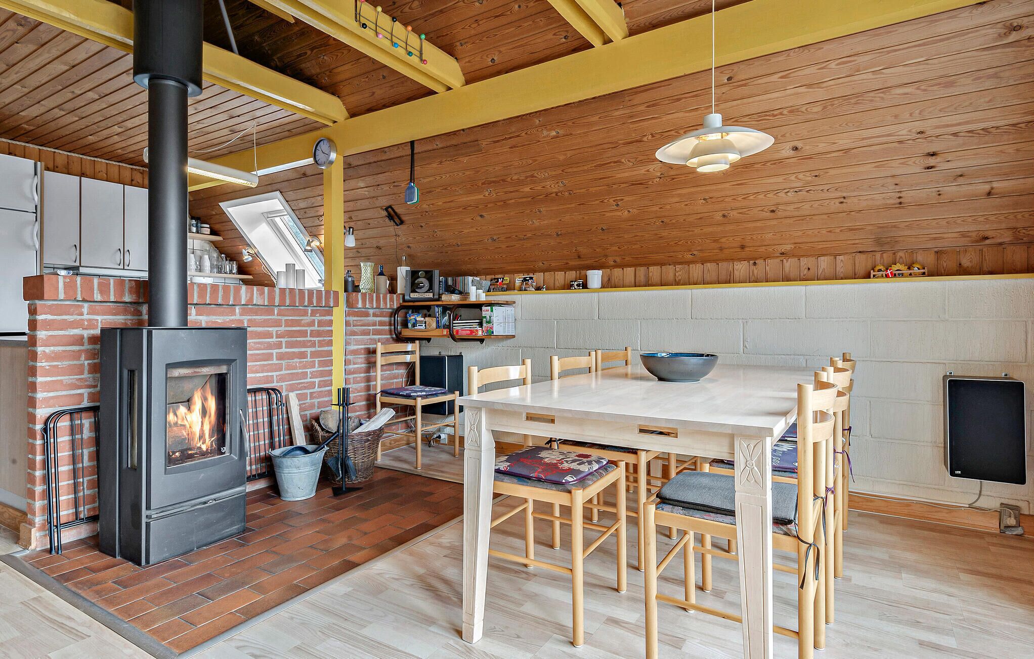 Una cocina acogedora con estufa de leña, una mesa de comedor con sillas y una lámpara colgante.