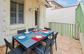 Une table à manger dressée pour quatre personnes, avec des chaises, une fenêtre et, au fond, un portail vert.