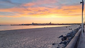 Une plage bordée d’une côte rocheuse, un phare et une grande roue visible au loin.