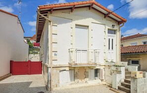 Un immeuble de deux étages doté d’un balcon, d’une porte de garage rouge et d’un petit porche à l’avant.