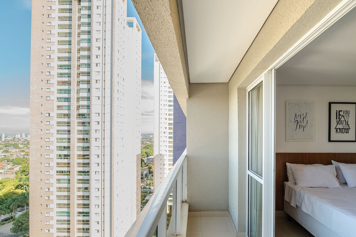 A balcony with a city view, a bed with white bedding, and two framed motivational quotes on the wall.
