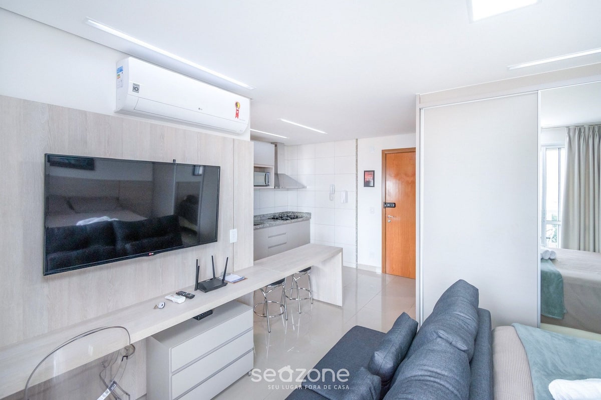 A modern living room with a flat-screen TV, a kitchen area, and a sofa.
