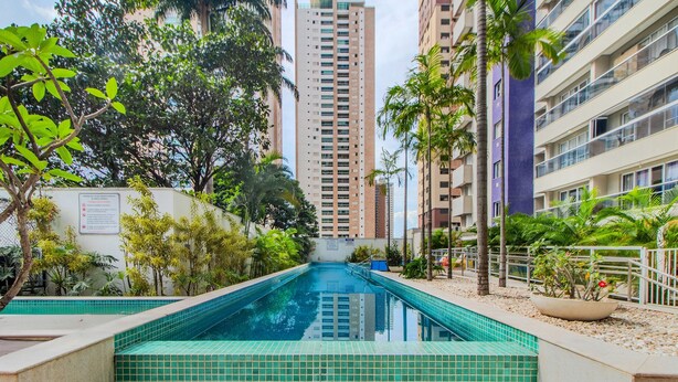 A swimming pool surrounded by greenery and tall buildings. - Charmosos Flats no Setor Bueno TXP (Goiânia)