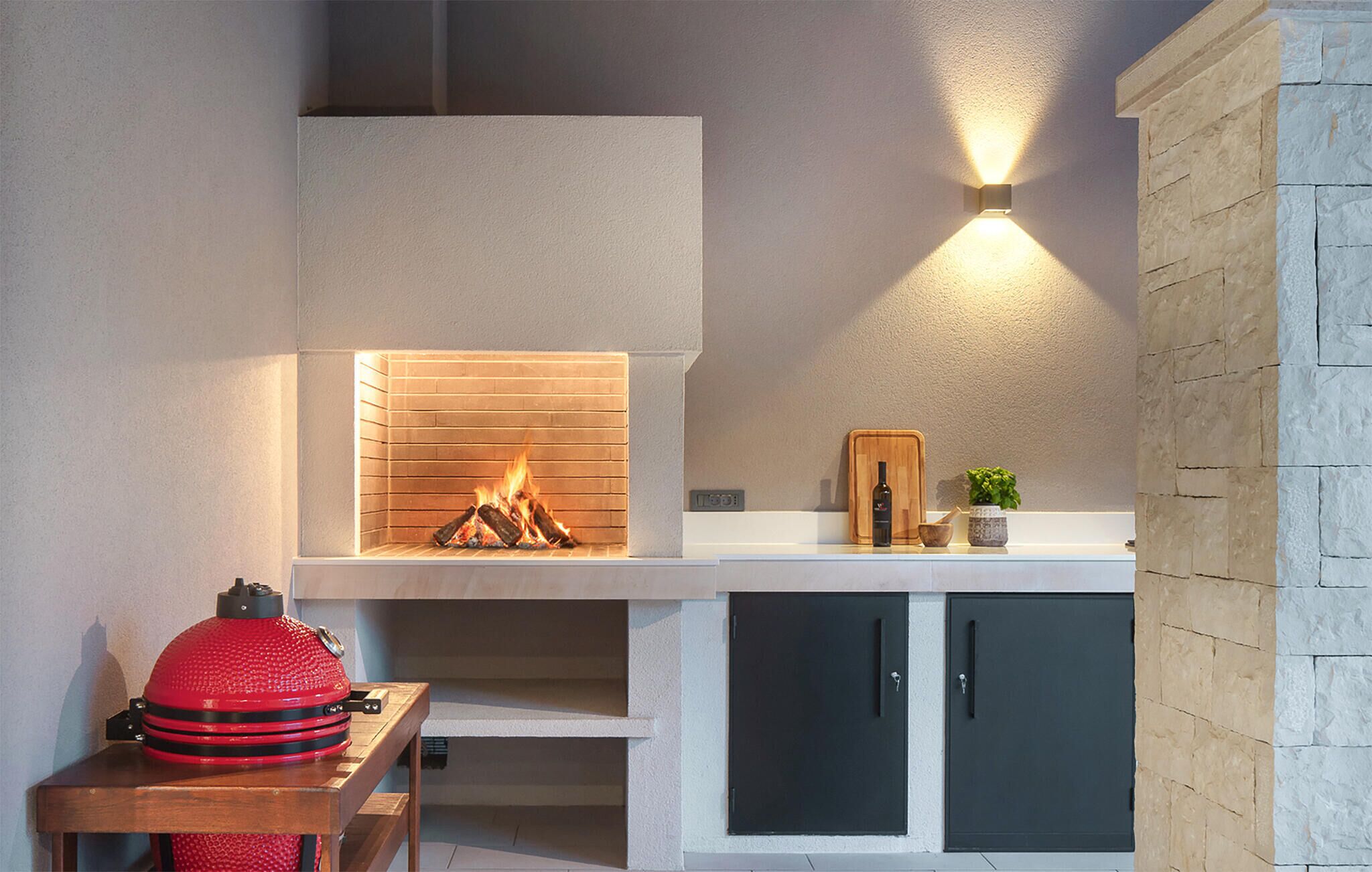 A modern kitchen with a built-in fireplace, a red grill, and a wall-mounted light fixture.