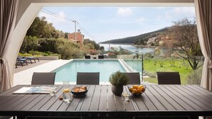 Terraza con piscina, mesa de comedor y sillas, con vistas a un río y colinas.