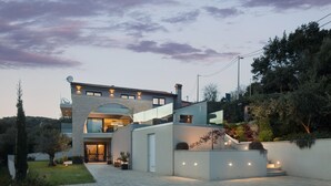 Una casa moderna de dos pisos con un amplio acceso de vidrio, un espacio exterior cubierto y un jardín ajardinado.