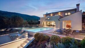 Una casa moderna con piscina, mobiliario exterior y vistas de las colinas circundantes.