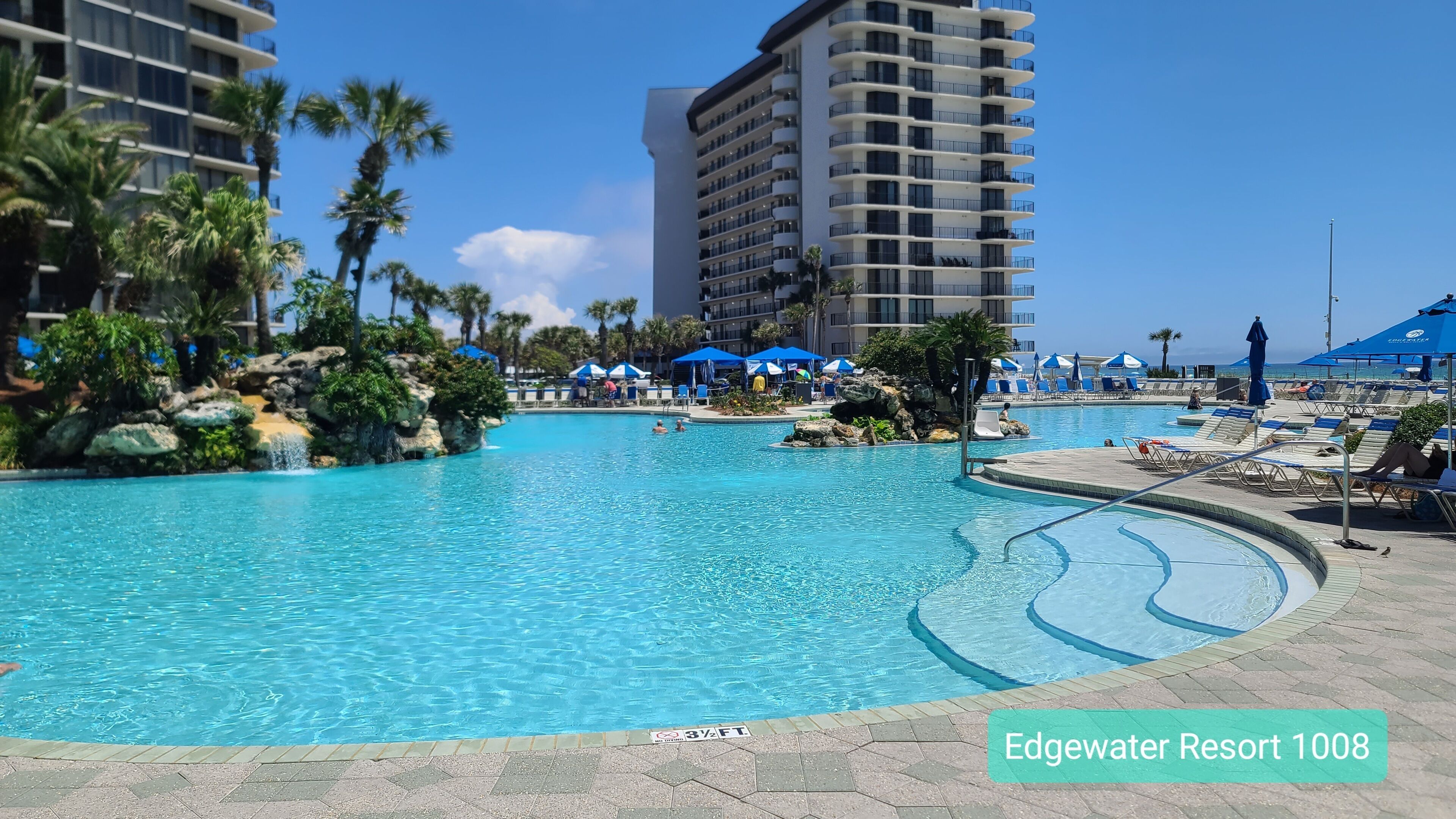 A resort pool with clear blue water, surrounded by palm trees and lounge chairs.