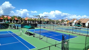 A tennis court complex with multiple courts, seating areas, and a net.