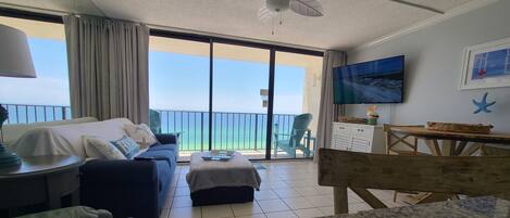 Una habitación con sofá, mesa de comedor, televisor y balcón con vista al mar.