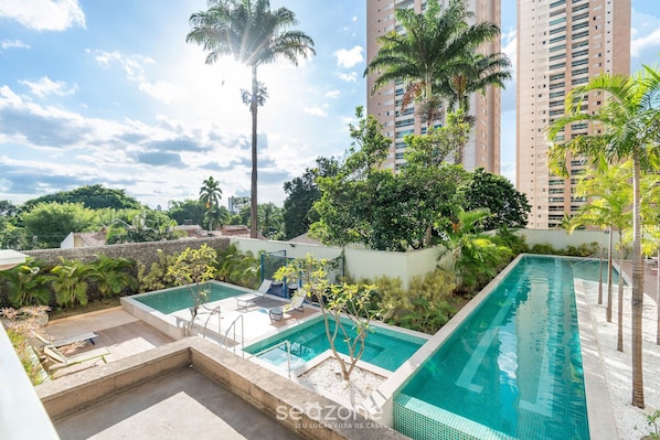 Una piscina en la azotea con sillas de descanso y palmeras.