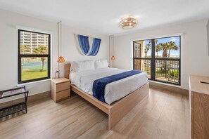 A modern bedroom with a large bed, wooden nightstands, a bench, and a view of a golf course through a window. - Saida II Beachfront Oasis (South Padre Island)