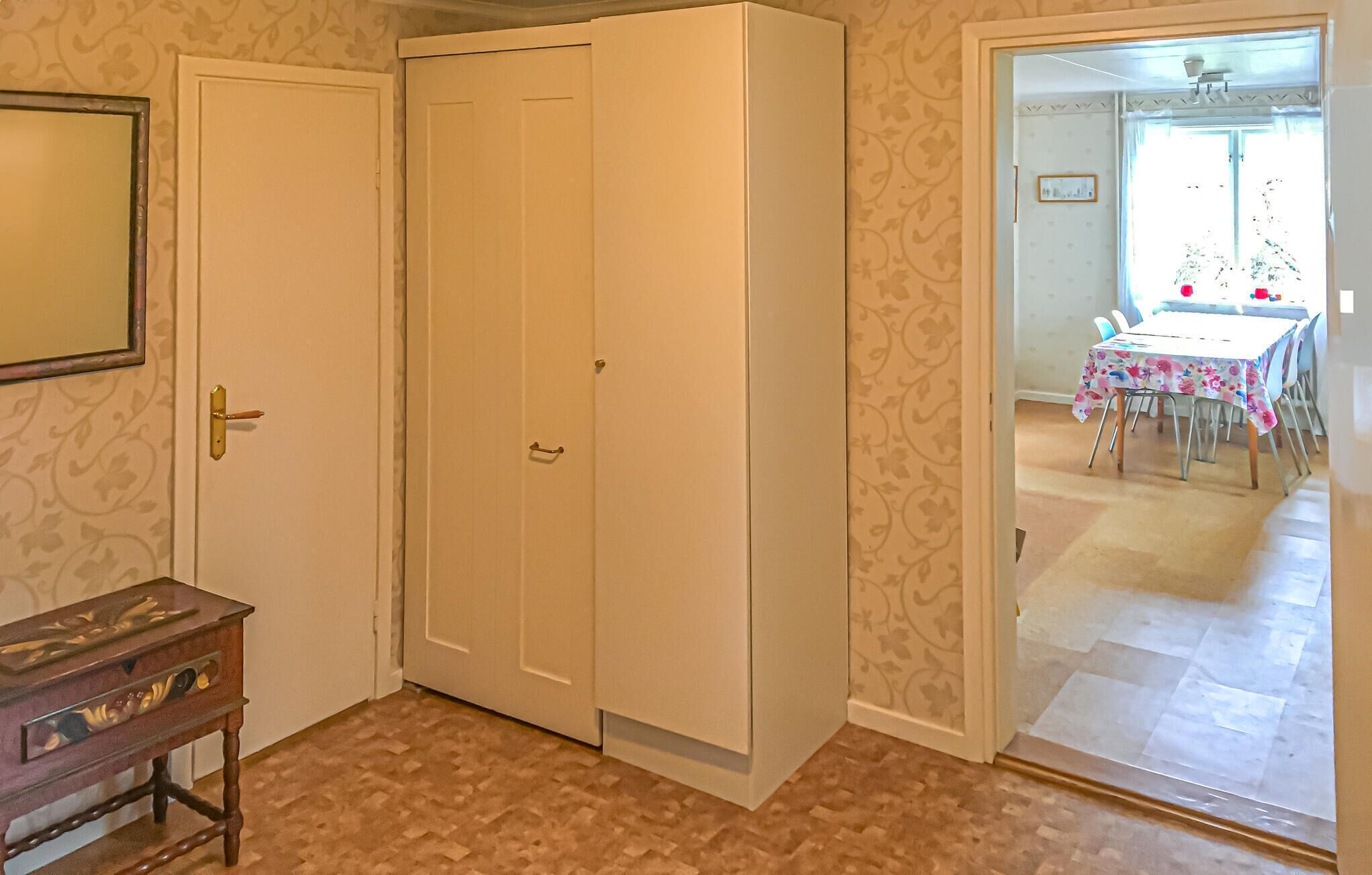 Une pièce avec une armoire blanche fermée, une table d’appoint en bois dotée de tiroirs et un tapis à motifs.