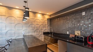A modern kitchen with a black countertop, a built-in coffee machine, and a tiled backsplash. - Modernos Flats no Setor Bueno TXP03 (Goiânia)