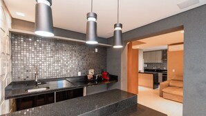 A modern kitchen with a black countertop, a tiled backsplash, and pendant lighting. - Modernos Flats no Setor Bueno TXP03 (Goiânia)