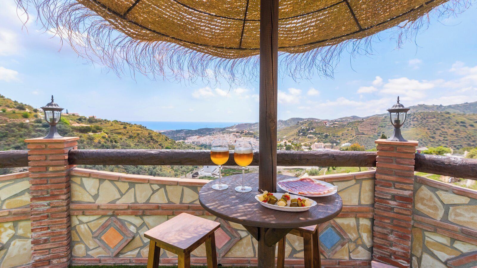 A terrace with a table set for two, a plate of tapas, and two glasses of beer, overlooking a scenic landscape.