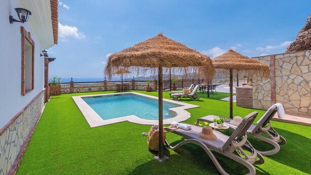 A pool area with artificial grass, lounge chairs, and thatched umbrellas. - Casa La Solana Torrox by Ruralidays (Málaga)