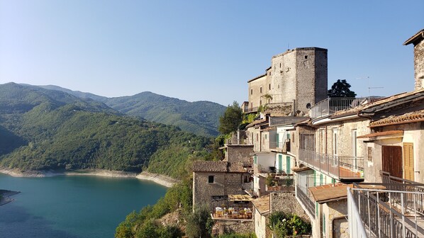 A coastal village with stone buildings, a tower, and a view of the sea and mountains.