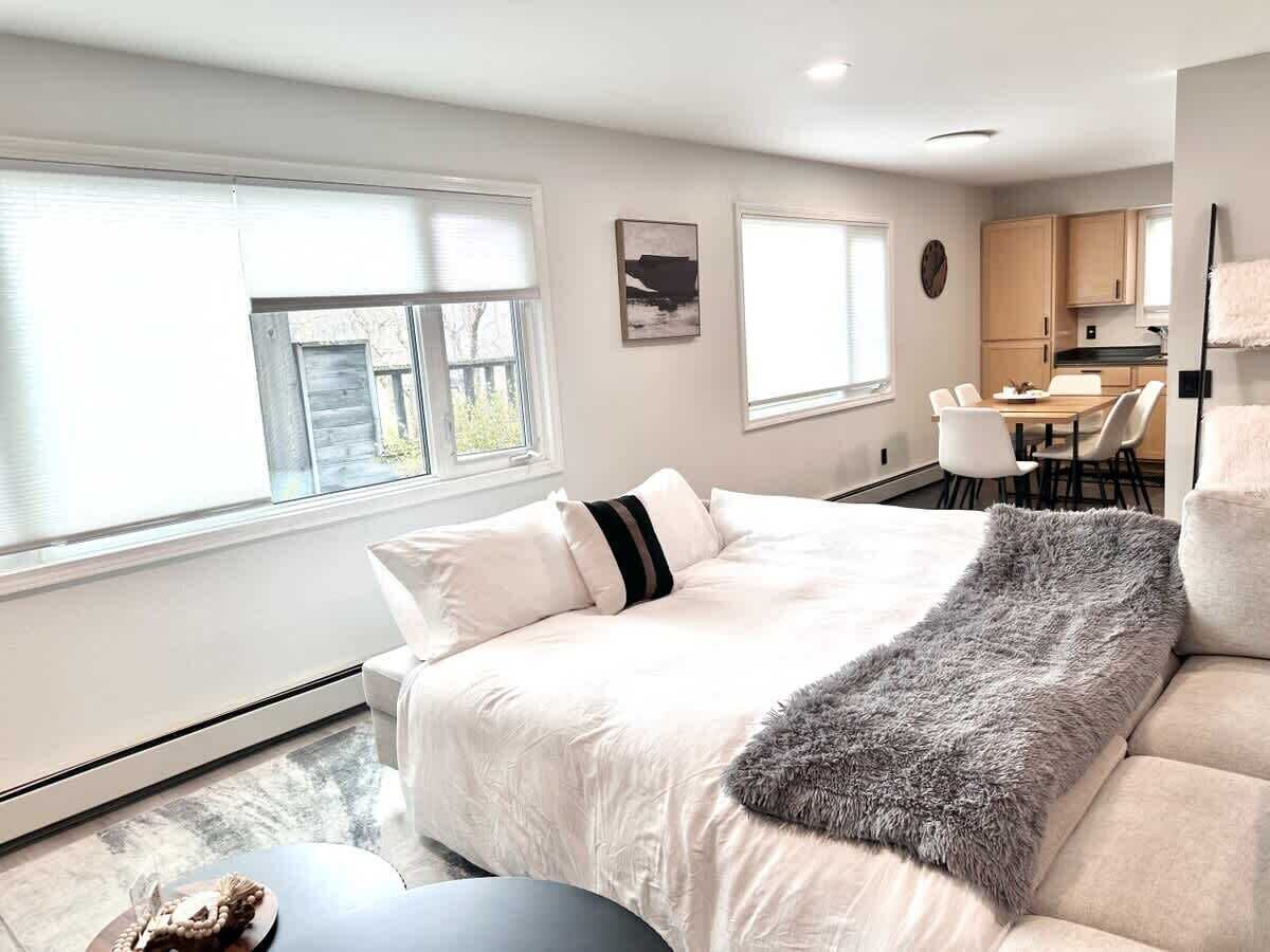 Ein modernes Schlafzimmer mit einem großen Bett, einer grauen Tagesdecke und einer Essecke mit Stühlen und einem Tisch.