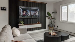 Un salon moderne avec un canapé gris, une table basse noire et un grand téléviseur fixé sur un mur foncé.