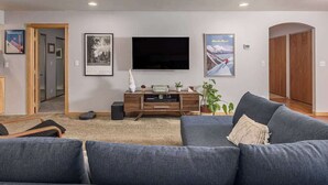 Una sala de estar moderna con un sofá gris, un televisor de pantalla plana montado en la pared y un mueble de entretenimiento de madera con objetos decorativos.
