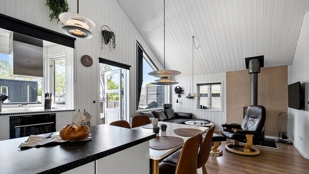 A modern kitchen with a central island, dining area with chairs, a sofa, and a fireplace.