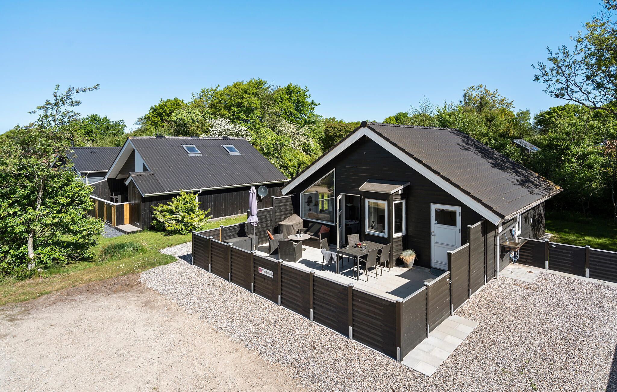 A modern cabin with a patio area, a separate entrance, and a large window overlooking the surrounding greenery.