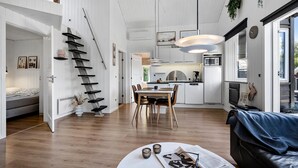 A modern kitchen with white cabinets, a dining area with a wooden table and chairs, and a staircase with black steps.