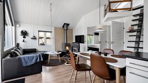 A modern, compact living space with a dining area, a fireplace, and a loft bedroom.